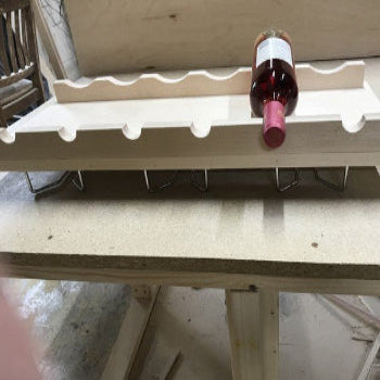 Wooden adjustable wine bottle shelf with slots holding a single wine bottle on a workshop table
