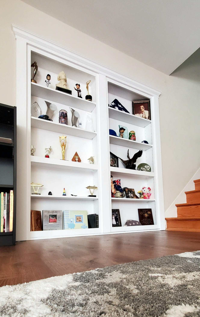 White hidden bookcase door filled with decorative items in a room with wooden floor and staircase.