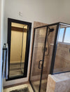 Hidden mirror door with black frame installed on bathroom wall next to glass shower enclosure