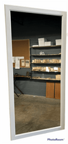 Full length wall mirror with white frame reflecting a workshop with shelves and real wood lower cabinet doors