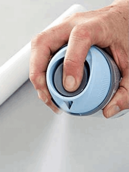 Hand pressing blue spray can nozzle applying touch-up spray for wood doors on white surface