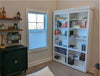 White bi-fold bookcase door with multiple shelves filled with books in a cozy room corner