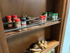 Wooden spice rack shelves holding various spice jars with metal railings inside a wooden cabinet