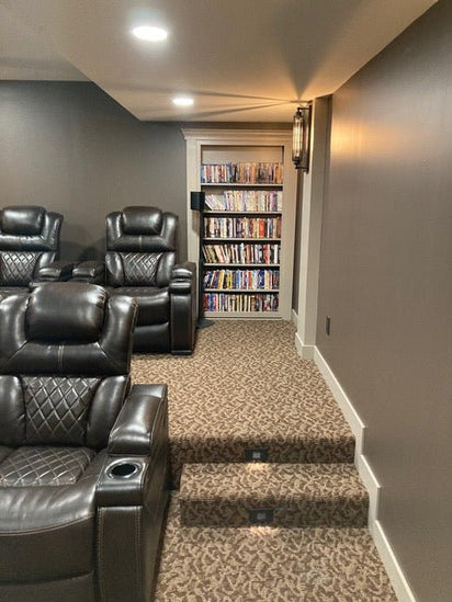 Cozy home theater room with leather recliners and a hidden door bookcase filled with DVDs