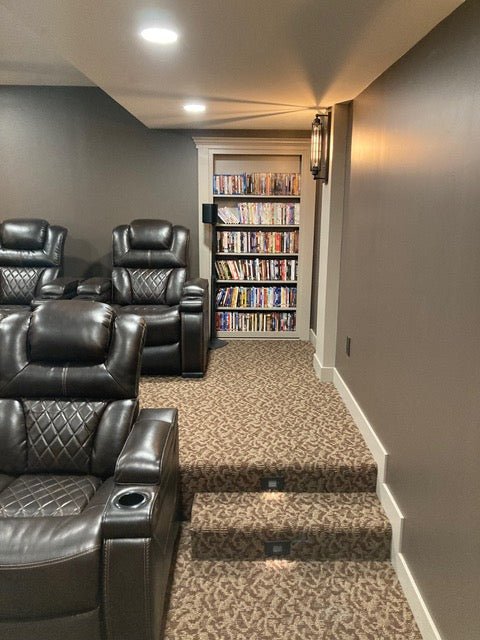 Cozy home theater room with leather recliners and a hidden door bookcase filled with DVDs